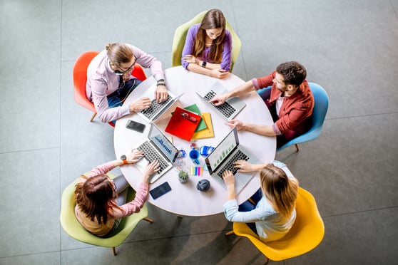 Team of a young coworkers working together with laptops sitting at the round table in the office