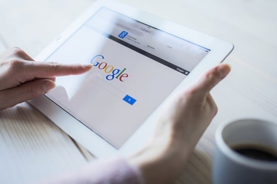 Image of a person holding a tablet, with the Google search engine open on the screen.