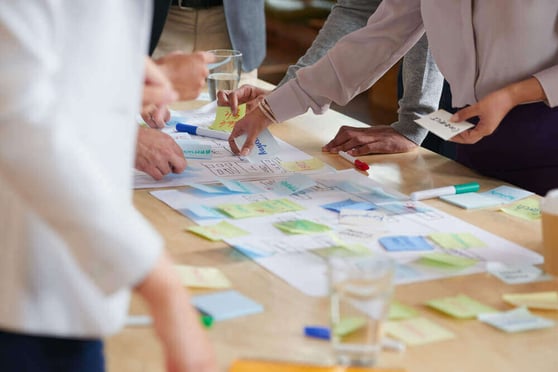 Image of people standing over a long table, with a lot of sticky notes stuck on it.