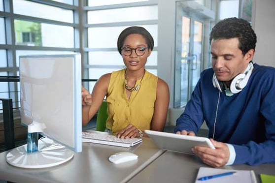 Two marketing professionals collaborating on email marketing services using computer and tablet devices.