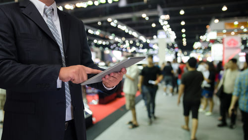 Businessman using tablet with blurred event background, illustrating experiential marketing in action.